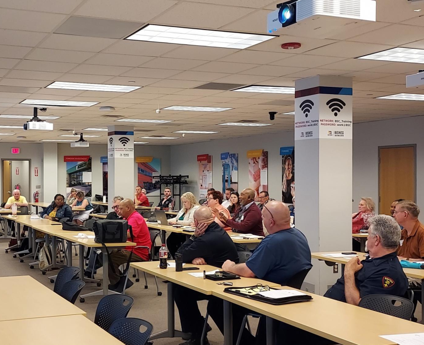 People sitting at tables and chairs in a workshop listening to a speaker