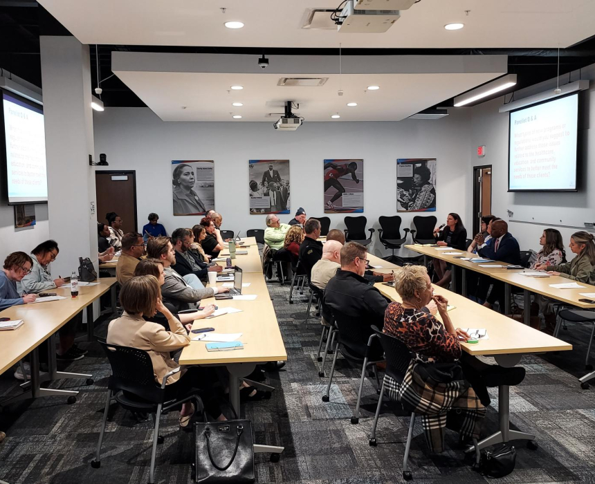 People sitting at tables in a workshop setting listening to a speaker