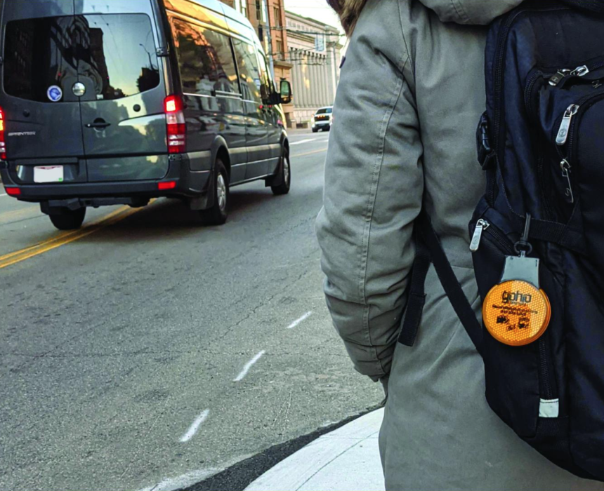 A person wearing a backpack walking along the side of a city street as a van passes by