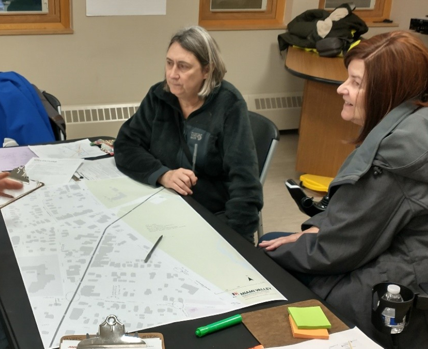 three people sit around a table in an office with planning documents laid out in front of them